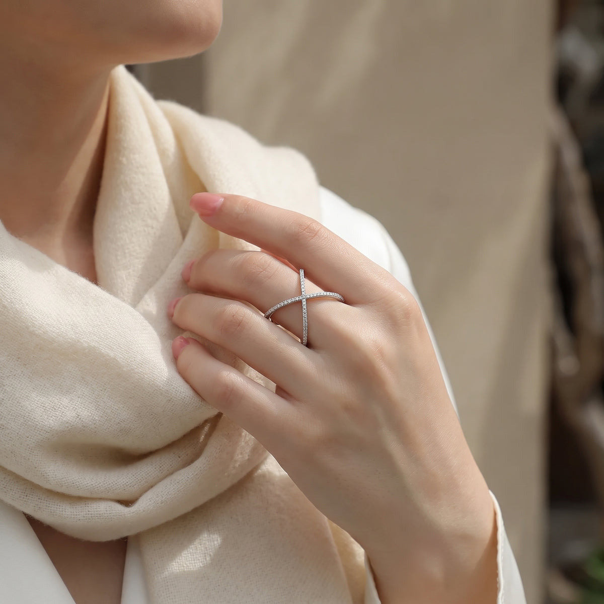 Vellmonto Axis silver moissanite crossover ring worn on a hand beside a cream scarf.